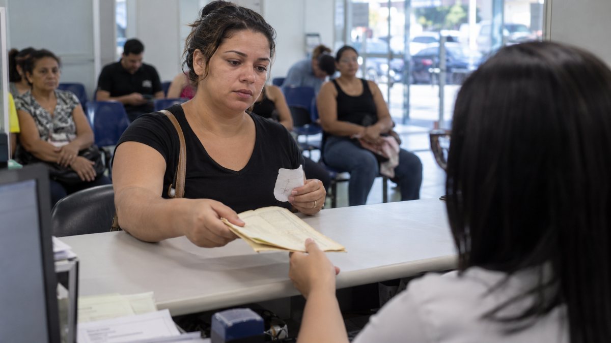 Como tirar a Carteira de Identidade Nacional (CIN) Mulher entrega certidão em guichê de posto de identificação para pedir a nova carteira de identidade